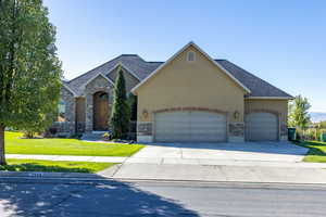 View of front of house with a front yard, stone siding, driveway, and stucco siding