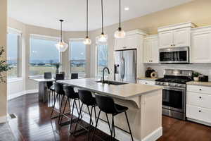 Kitchen featuring stainless steel appliances, a center island with sink, white cabinetry, decorative backsplash, and hanging light fixtures