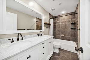 Full bathroom with double vanity, shower / tub combo, and dark tile patterned flooring