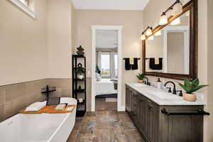 Bathroom with double vanity, a soaking tub, ensuite bathroom, tile walls, and stone tile floors