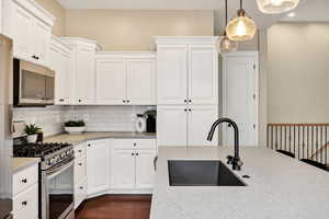 Kitchen with stainless steel appliances, hanging light fixtures, white cabinetry, tasteful backsplash, and light stone counters