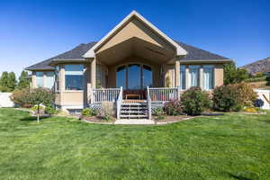 Back of house with stucco siding, a porch, a yard, and roof with shingles