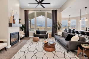 Living area with a glass covered fireplace, a ceiling fan, light carpet, healthy amount of natural light, and recessed lighting