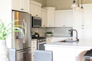 Kitchen with appliances with stainless steel finishes, decorative light fixtures, white cabinets, a kitchen bar, and tasteful backsplash