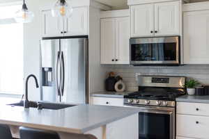 Kitchen with stainless steel appliances, white cabinets, backsplash, a breakfast bar area, and an island with sink