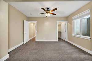 Unfurnished bedroom featuring dark carpet, a spacious closet, and a ceiling fan