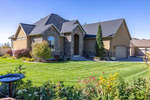 View of front facade featuring stone siding, a front yard, and stucco siding