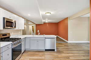 Kitchen with stainless steel appliances, light countertops, a peninsula, gray cabinetry, and white cabinetry