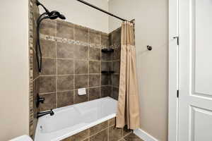 Full bath featuring tiled shower / bath combo and baseboards