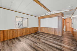 Empty room featuring wood walls, a wainscoted wall, wood finished floors, and crown molding