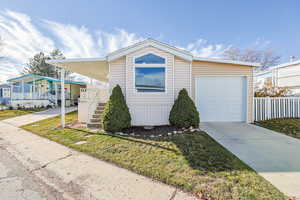 Manufactured / mobile home with concrete driveway, covered porch, a front lawn, and stairway