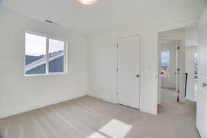 Unfurnished bedroom featuring light carpet and multiple windows