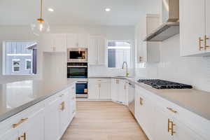 Kitchen with white cabinetry, wall chimney exhaust hood, light stone countertops, stainless steel appliances, and recessed lighting