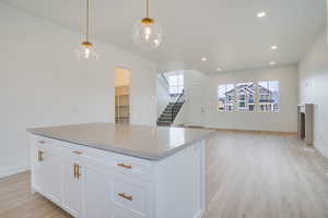 Kitchen featuring white cabinetry, pendant lighting, open floor plan, light wood-style flooring, and a center island