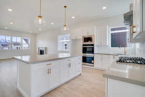 Kitchen featuring white cabinetry, light stone counters, open floor plan, a center island, and appliances with stainless steel finishes