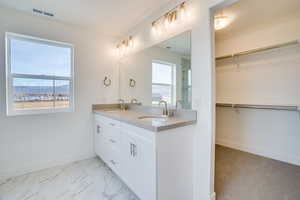 Full bathroom with a spacious closet, double vanity, a marble finish shower, and light marble finish flooring