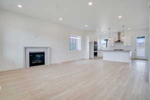 Unfurnished living room with light wood-style floors, recessed lighting, and a glass covered fireplace