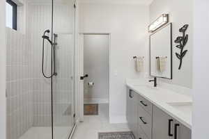 Bathroom with double vanity, tiled shower, and light tile patterned floors