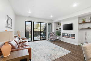 Living room featuring dark wood finished floors, a glass covered fireplace, built in shelves, and recessed lighting