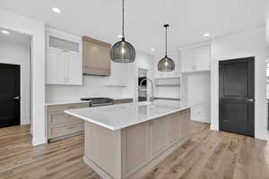 Kitchen with custom exhaust hood, a center island with sink, decorative light fixtures, light wood finished floors, and gas stove
