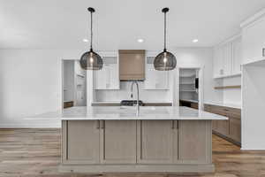 Kitchen featuring white cabinets, a center island with sink, light stone counters, light wood-style floors, and tasteful backsplash