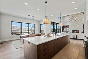 Kitchen with a chandelier, a stone fireplace, light stone countertops, light wood-style flooring, and recessed lighting