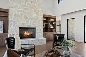 Living area featuring a stone fireplace, wood finished floors, and a high ceiling