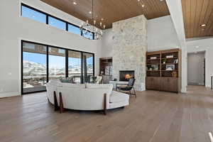 Living area featuring a mountain view, a stone fireplace, light wood-type flooring, wooden ceiling, and a high ceiling