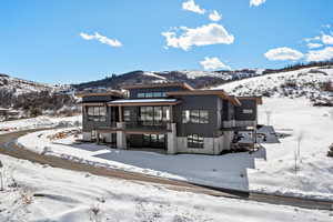 Snow covered back of property featuring stone siding, a balcony, and a mountain view