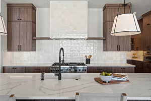 Kitchen with light stone counters, open shelves, wall chimney range hood, hanging light fixtures, and stainless steel oven