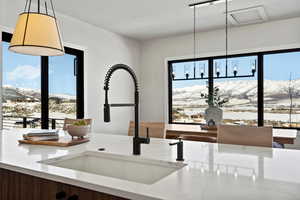 Kitchen view of a mountain backdrop, light stone countertops, and hanging light fixtures