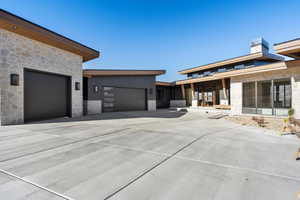 Exterior space featuring stone siding, driveway, an attached garage, and a chimney