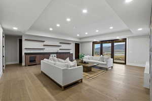 Living area featuring a raised ceiling, light wood-style floors, bar with sink, recessed lighting, and beverage cooler