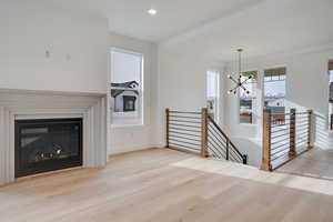 Unfurnished living room featuring light wood-style floors, a chandelier, a glass covered fireplace, and recessed lighting