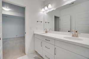 Bathroom with double vanity, light carpet, and light marble finish floors