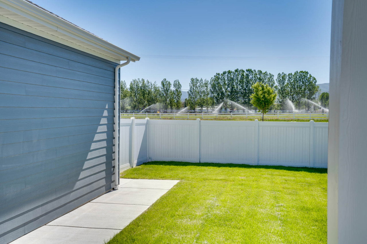 Expansive backyard featuring a manicured lawn, concrete walkway, and a white privacy fence