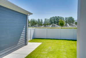 Expansive backyard featuring a manicured lawn, concrete walkway, and a white privacy fence