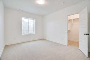 Unfurnished bedroom with a spacious closet and light carpet