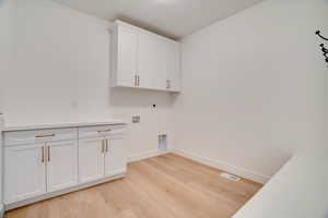 Laundry area featuring hookup for a washing machine, electric dryer hookup, light wood-style floors, and cabinet space