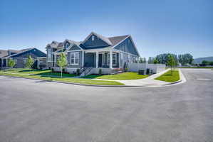 Corner lot property featuring dark blue siding with white trim, a covered front porch, a gabled roofline, and a manicured lawn