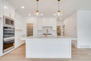 Kitchen with light stone countertops, appliances with stainless steel finishes, a kitchen island with sink, white cabinets, and recessed lighting