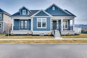 View of front facade with covered porch, a shingled roof, a front lawn, and board and batten siding