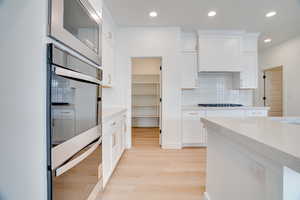Kitchen featuring backsplash, stainless steel appliances, light stone counters, light wood-style flooring, and white cabinets