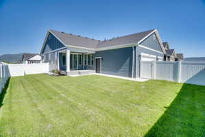 Expansive backyard featuring a lush lawn, white privacy fencing, and a covered patio with sliding glass doors