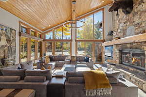 Living room featuring high vaulted ceiling, wood ceiling, a stone fireplace, wood finished floors, and a chandelier