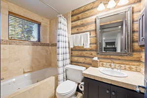 Full bathroom with vanity, log walls, and a combined bath / shower with jetted tub