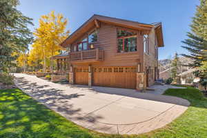 View of side of property with stone siding, a balcony, a lawn, a garage, and driveway