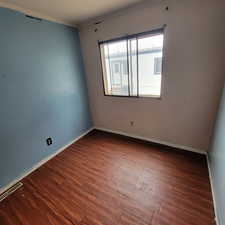 Empty room featuring dark wood-style flooring and crown molding