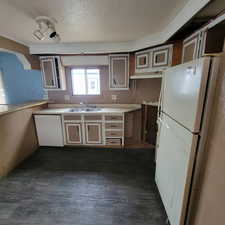 Kitchen featuring white appliances, light countertops, a textured ceiling, ornamental molding, and dark wood-type flooring