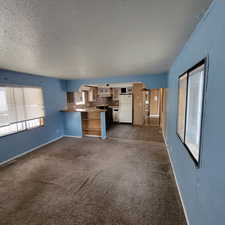 Kitchen with freestanding refrigerator, a textured ceiling, dark carpet, a peninsula, and arched walkways